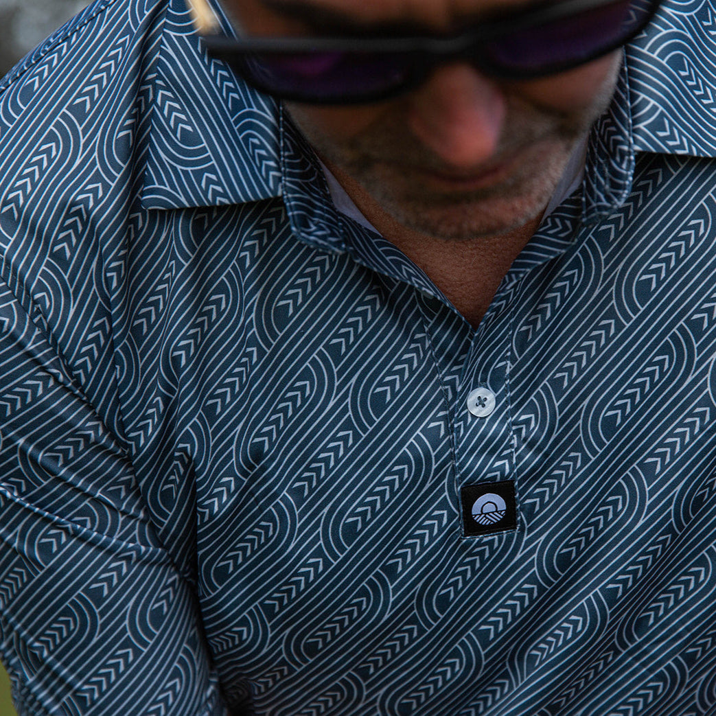 Pakati Men’s Golf Polo in dark grey with Māori-inspired geometric design. NZ golf shirt made from breathable, quick-dry performance fabric.