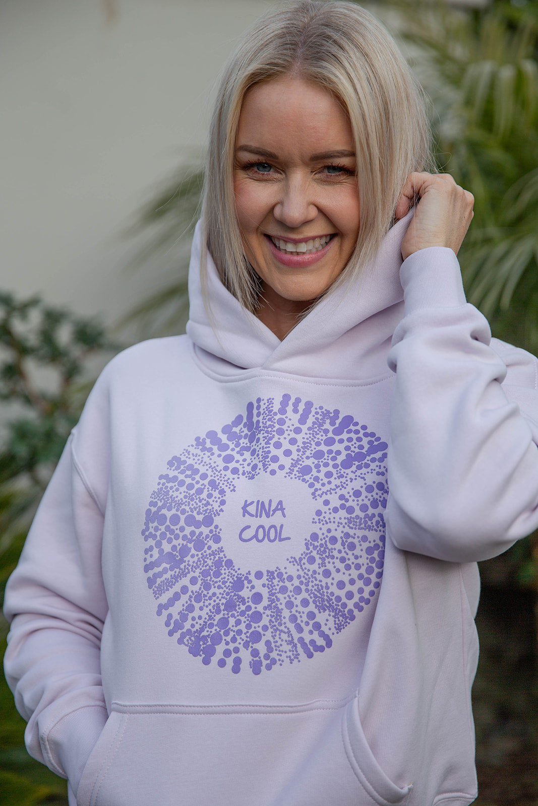 Woman wearing Kina Cool women’s relaxed fit hoodie in pastel purple with kina shell design, New Zealand casual streetwear