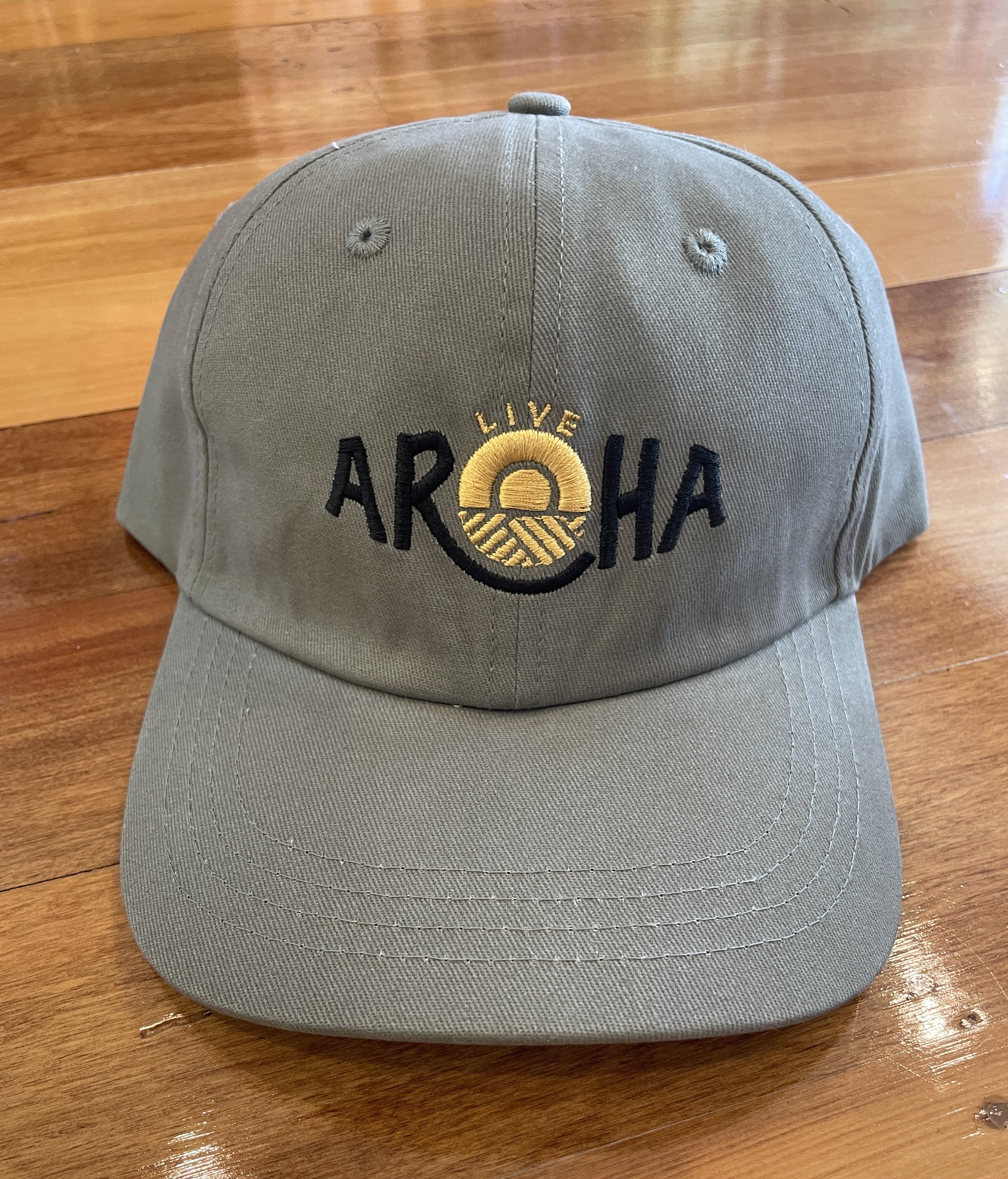 Olive green Live AROHA Cap with embroidered gold sun and bold black lettering. Stylish New Zealand lifestyle hat designed for everyday wear, outdoor adventures, and Kiwi summer fashion. Adjustable unisex cap offering comfort, durability, and a modern coastal look.