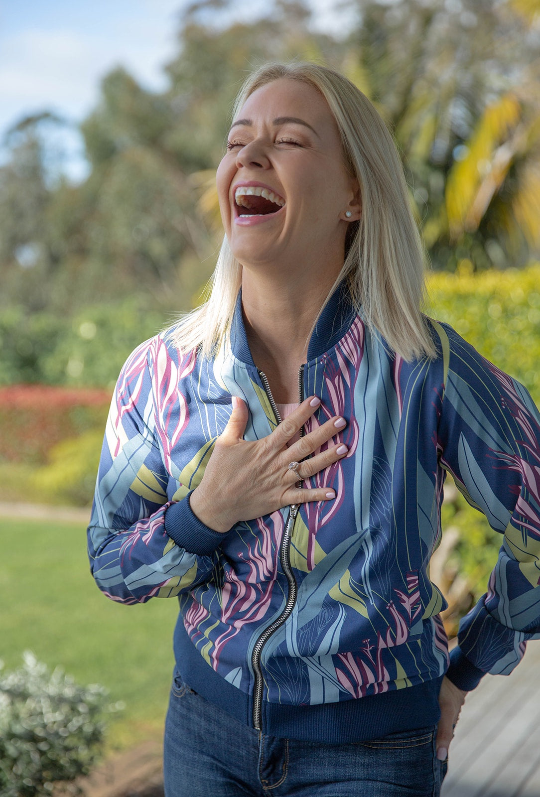 Woman laughing while wearing a Ladies Bomber Jacket in Blue Harakeke design, featuring New Zealand flax-inspired print, stylish and lightweight women’s outerwear