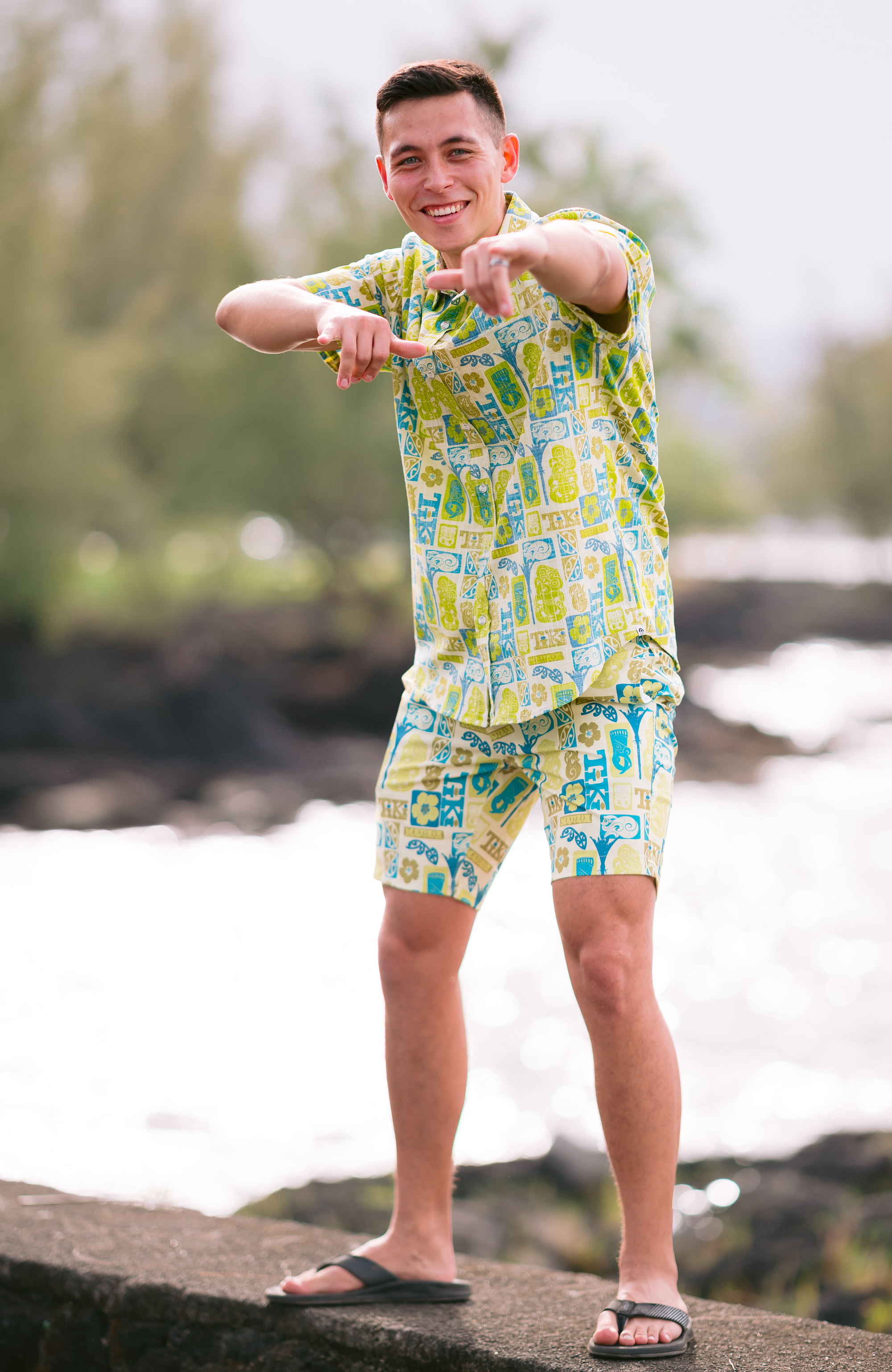 Men’s Tiki Manaia Kiwi Classic short sleeve shirt in vibrant green, blue, and yellow Polynesian-inspired print. Lightweight cotton blend perfect for summer, beach holidays, and New Zealand resort wear. Features bold tiki, manaia, and floral motifs for a unique island style.