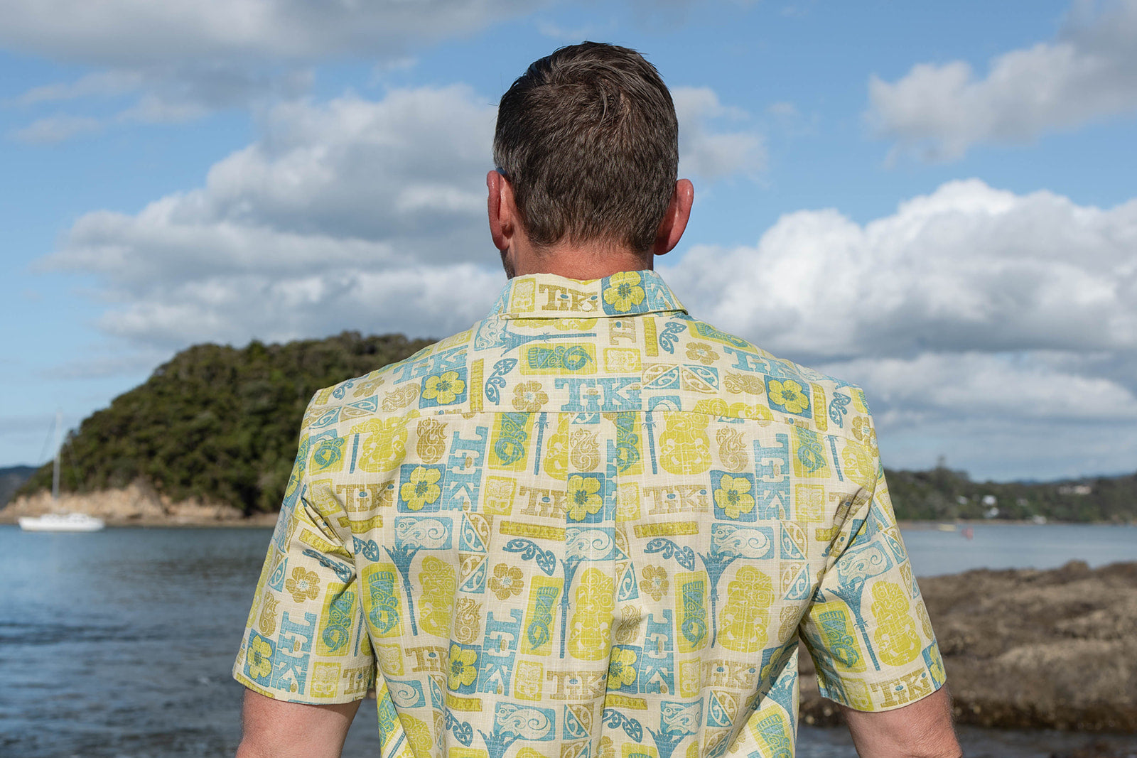 Men’s Tiki Manaia Kiwi Classic short sleeve shirt in vibrant green, blue, and yellow Polynesian-inspired print. Lightweight cotton blend perfect for summer, beach holidays, and New Zealand resort wear. Features bold tiki, manaia, and floral motifs for a unique island style.
