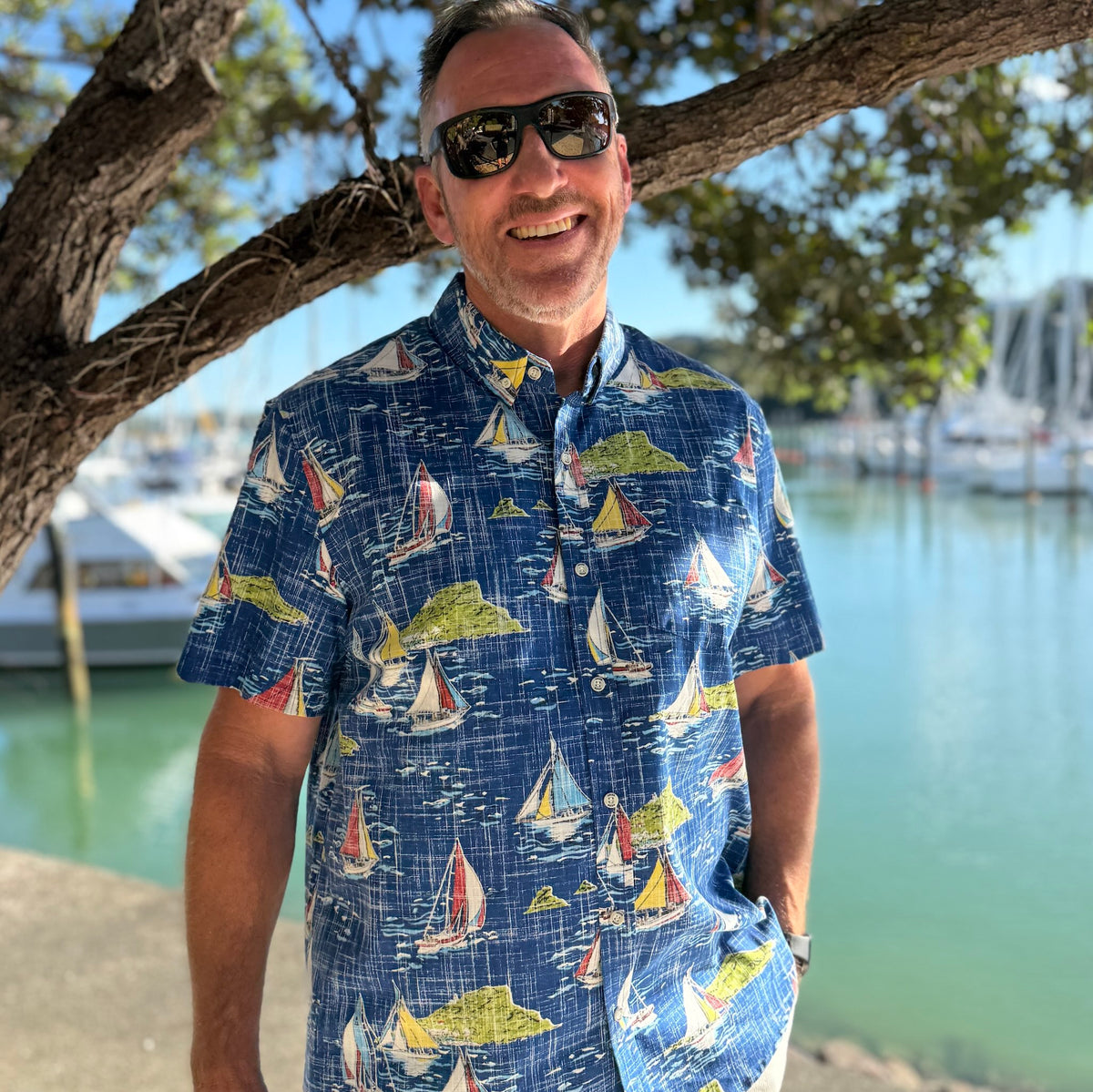 Sail the Bay Kiwi Classic men’s short sleeve shirt featuring classic New Zealand yachts on a blue background with primary colours , a real coastal print.