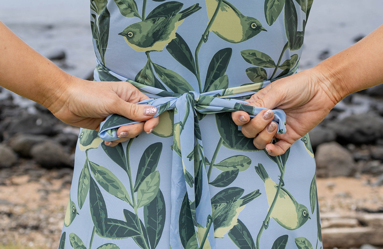 Elegant Tauhou / Wax-Eye wrap dress featuring a soft blue base with green wax-eye bird and foliage print. New Zealand-inspired women’s dress with flattering wrap design, short sleeves, and knee-length cut. Perfect for summer outings, coastal holidays, and everyday Kiwi style.