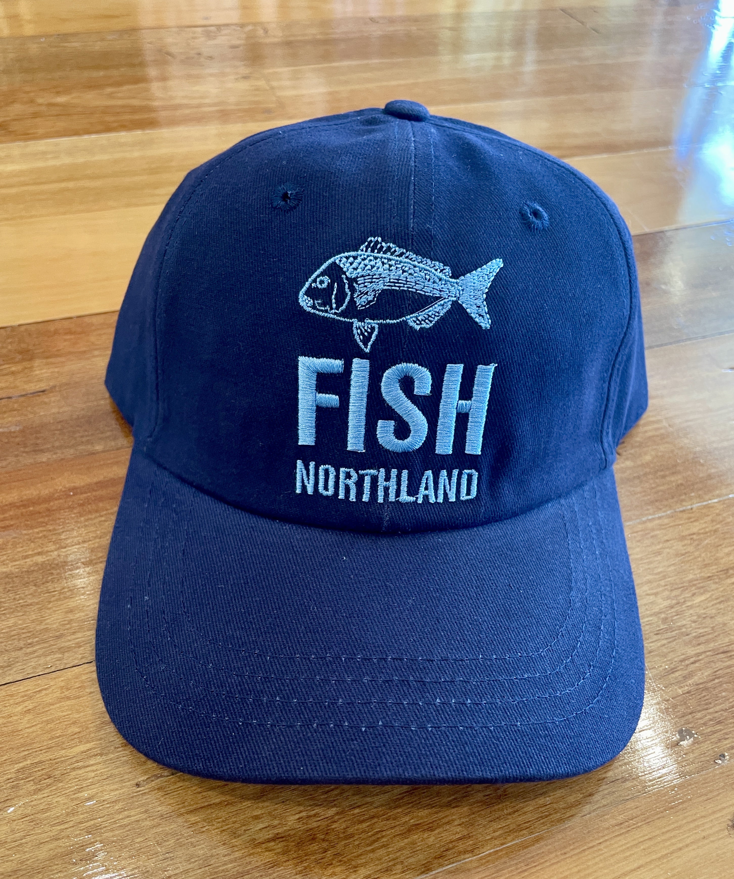 Navy blue FISH Northland Cap with embroidered snapper fish design and bold white lettering. Classic New Zealand fishing cap perfect for anglers, outdoor adventures, and Kiwi coastal lifestyle. Adjustable unisex hat offering comfort, durability, and sun protection.