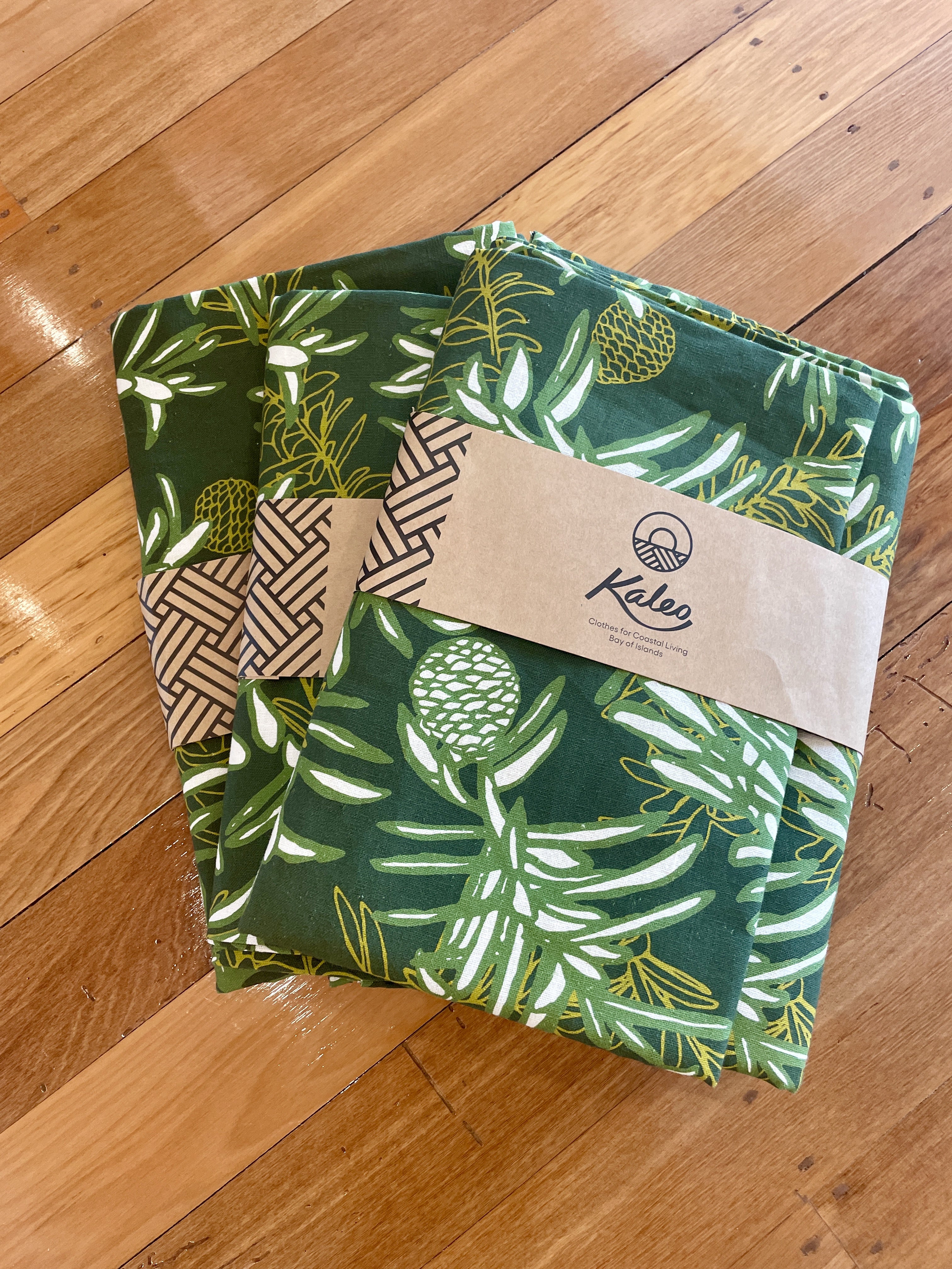 Folded green Kauri print tablecloth (140x260cm) by Kaleo. Features native New Zealand Kauri cone and foliage design. Perfect for dining tables, BBQs, Christmas gatherings, and everyday Kiwi home styling. Made from durable cotton fabric with a bold botanical print.