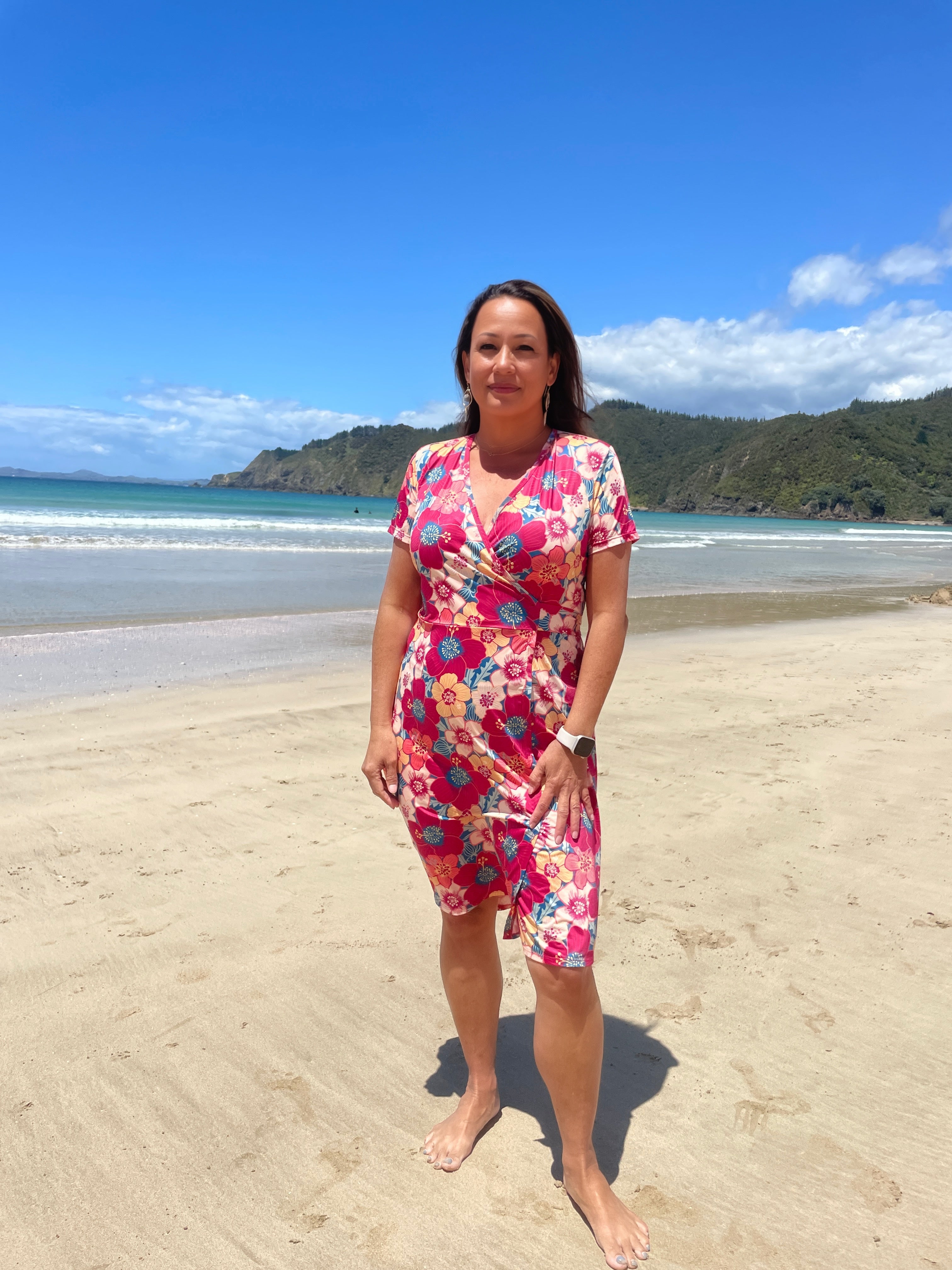 Vibrant Puarangi wrap dress in bold pink with red, yellow, and blue hibiscus-inspired floral print. Women’s short sleeve summer wrap dress, designed in New Zealand with a flattering fit and beach-to-evening style.