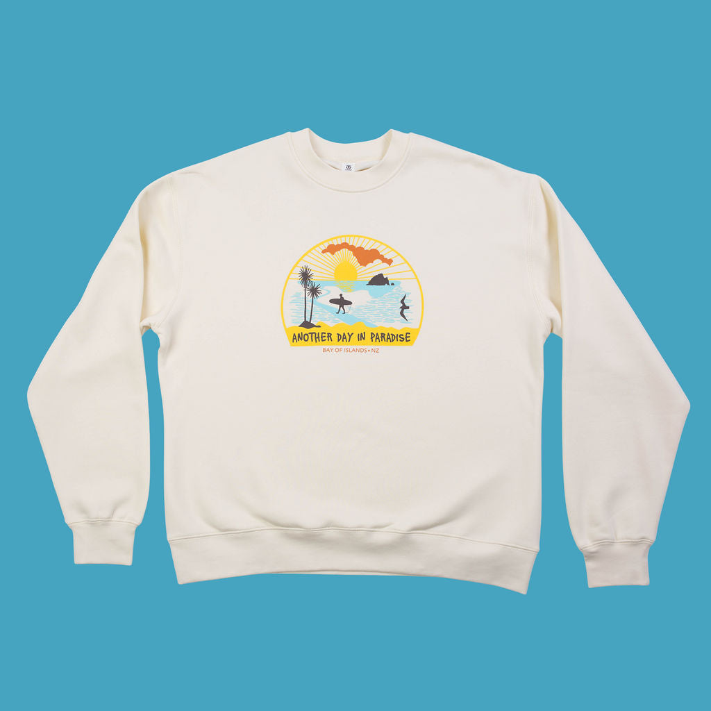Kaleo Another Day in Paradise sweatshirt, cream crewneck with Bay of Islands NZ print featuring surfers, sunset, and coastal design.